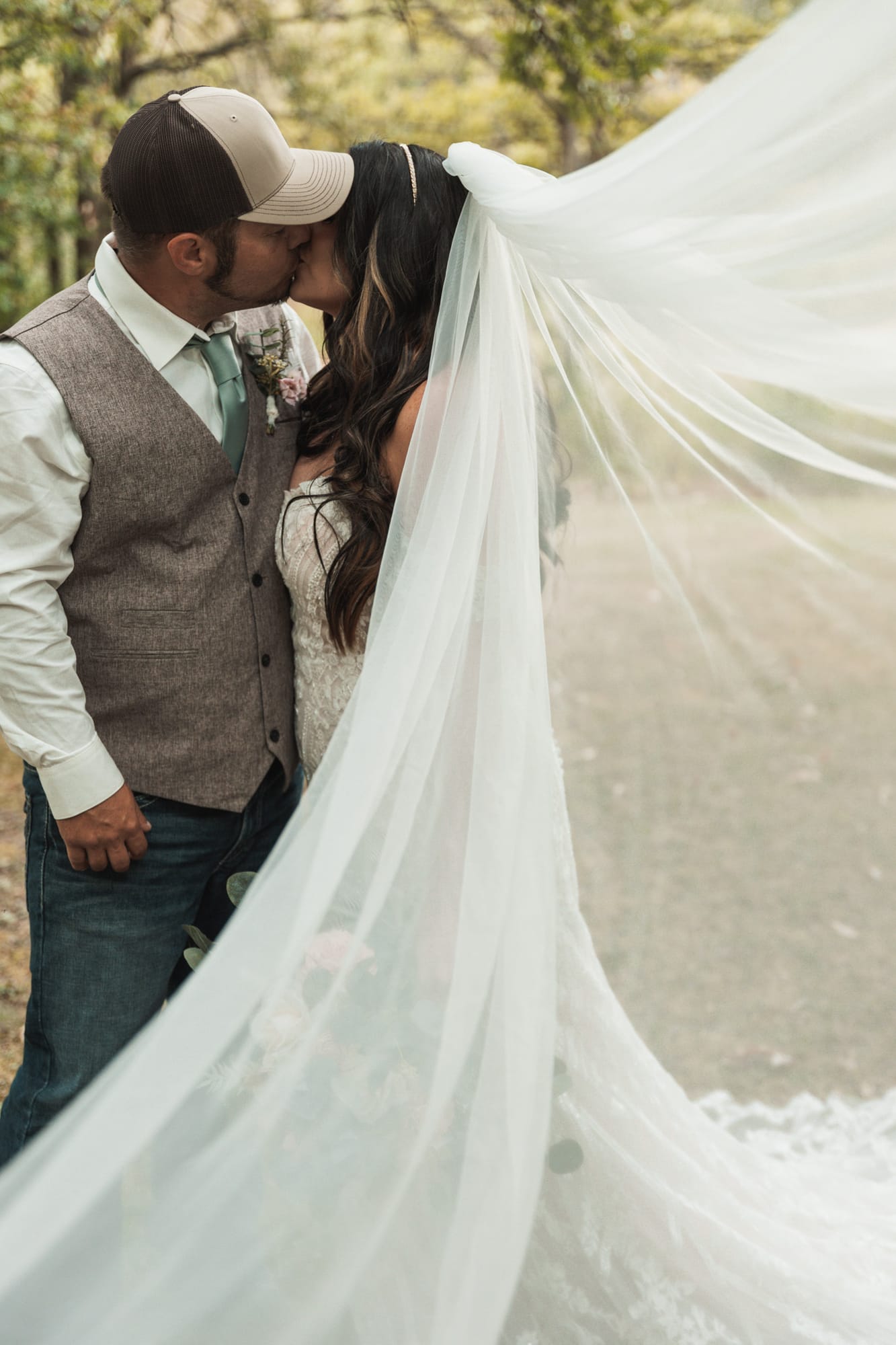 Rustic couple kissing beneath a long flowing veil